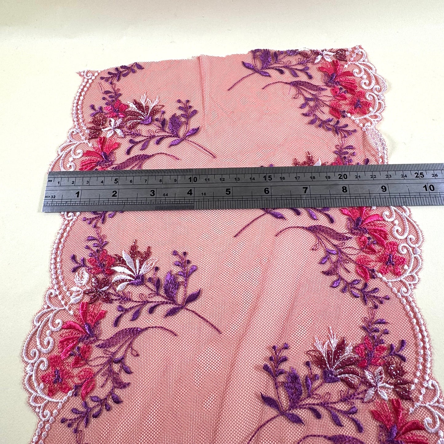 red galloon lace with red flowers, purple leaves and white embroidery at the edges . Ruler shows it as 23 cm width
