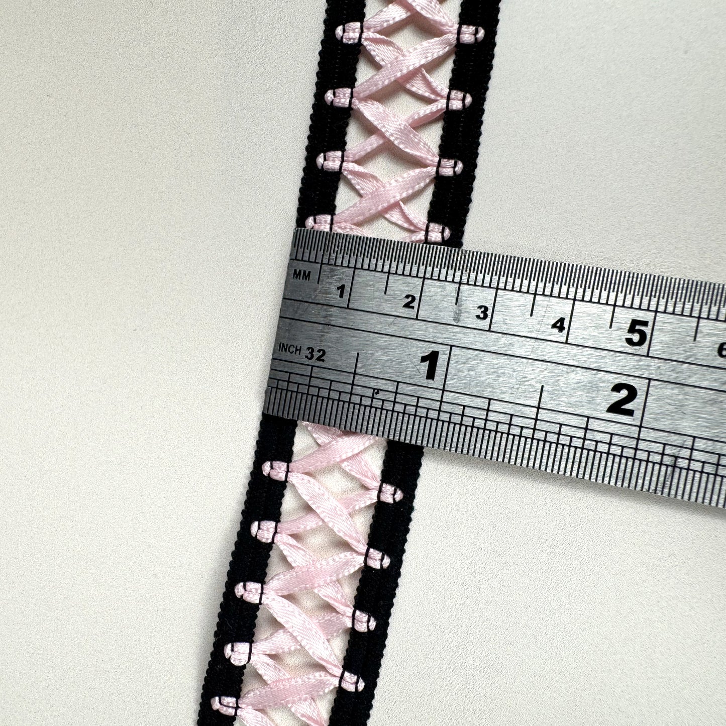 Close-up of pink laced fabric with a ruler for scale on a white background