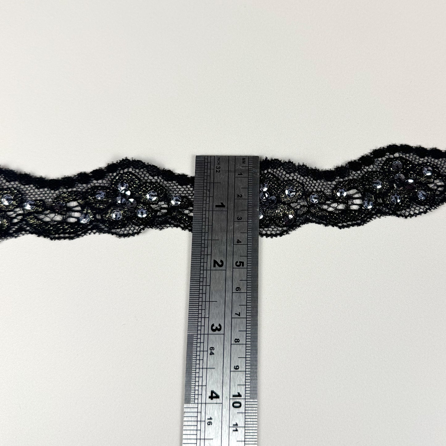 Black lace trim with a ruler for scale on a light background