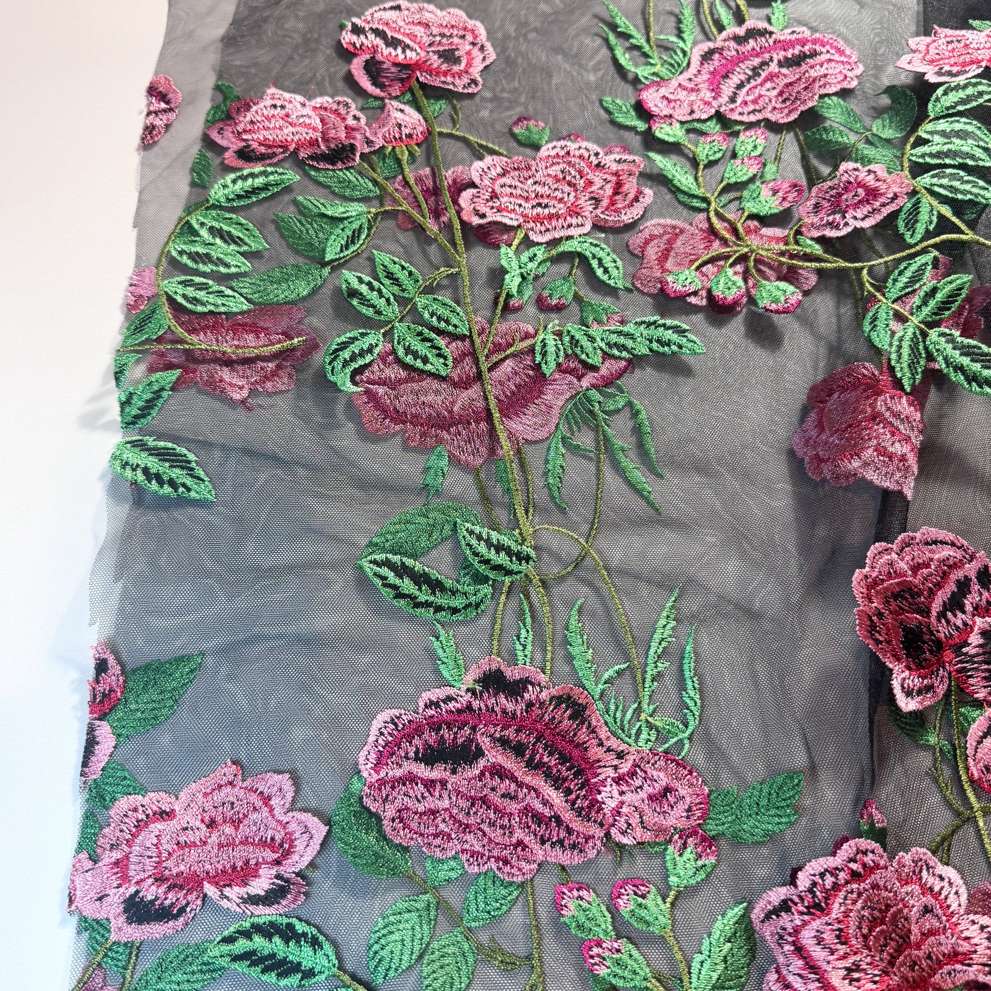 Black tulle with pink flowers and green leaves embroidered on to fabric