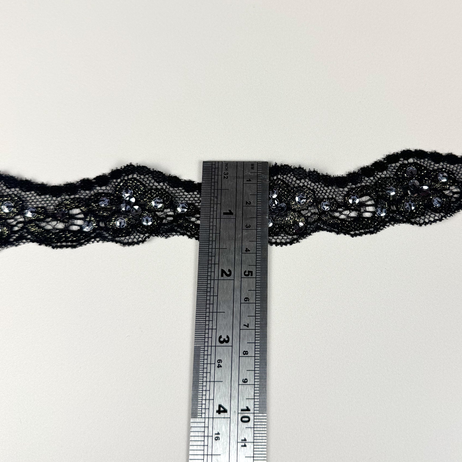 Black lace trim with a ruler for scale on a light background