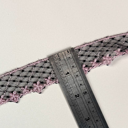 Close-up of lace trim with a ruler for measurement on a light background